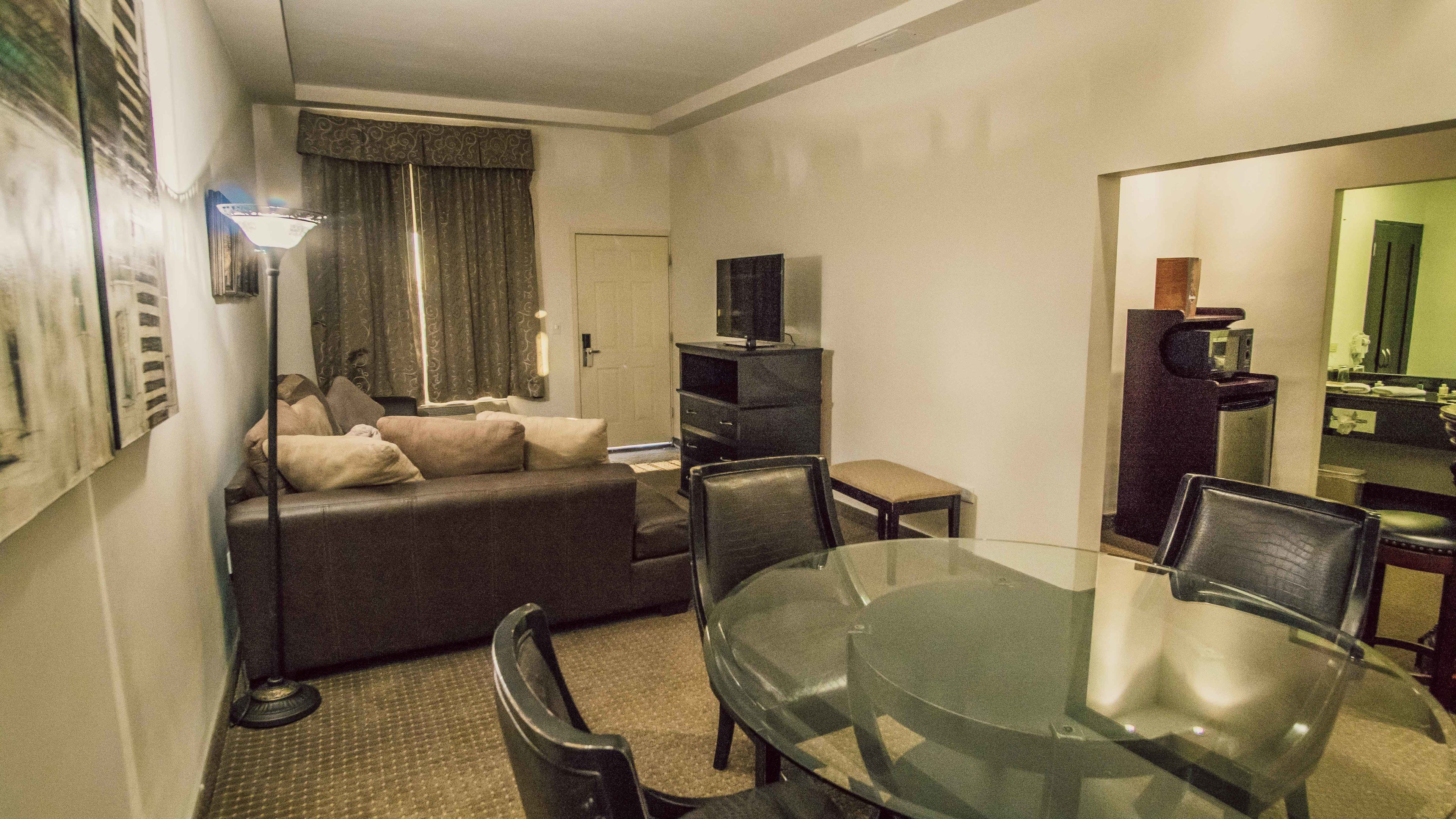 Una habitación de hotel compacta con sofá, una mesa de vidrio para comer y un televisor sobre un mueble.