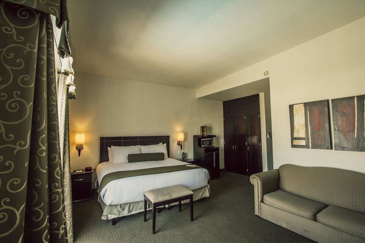 A hotel room with a bed, bedside tables, a bench, a sofa, and artwork on the wall.