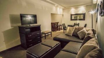 Una sala moderna con un sofá seccional, un televisor de pantalla plana, un mueble de entretenimiento de madera oscura y una zona de comedor con mesa y sillas.