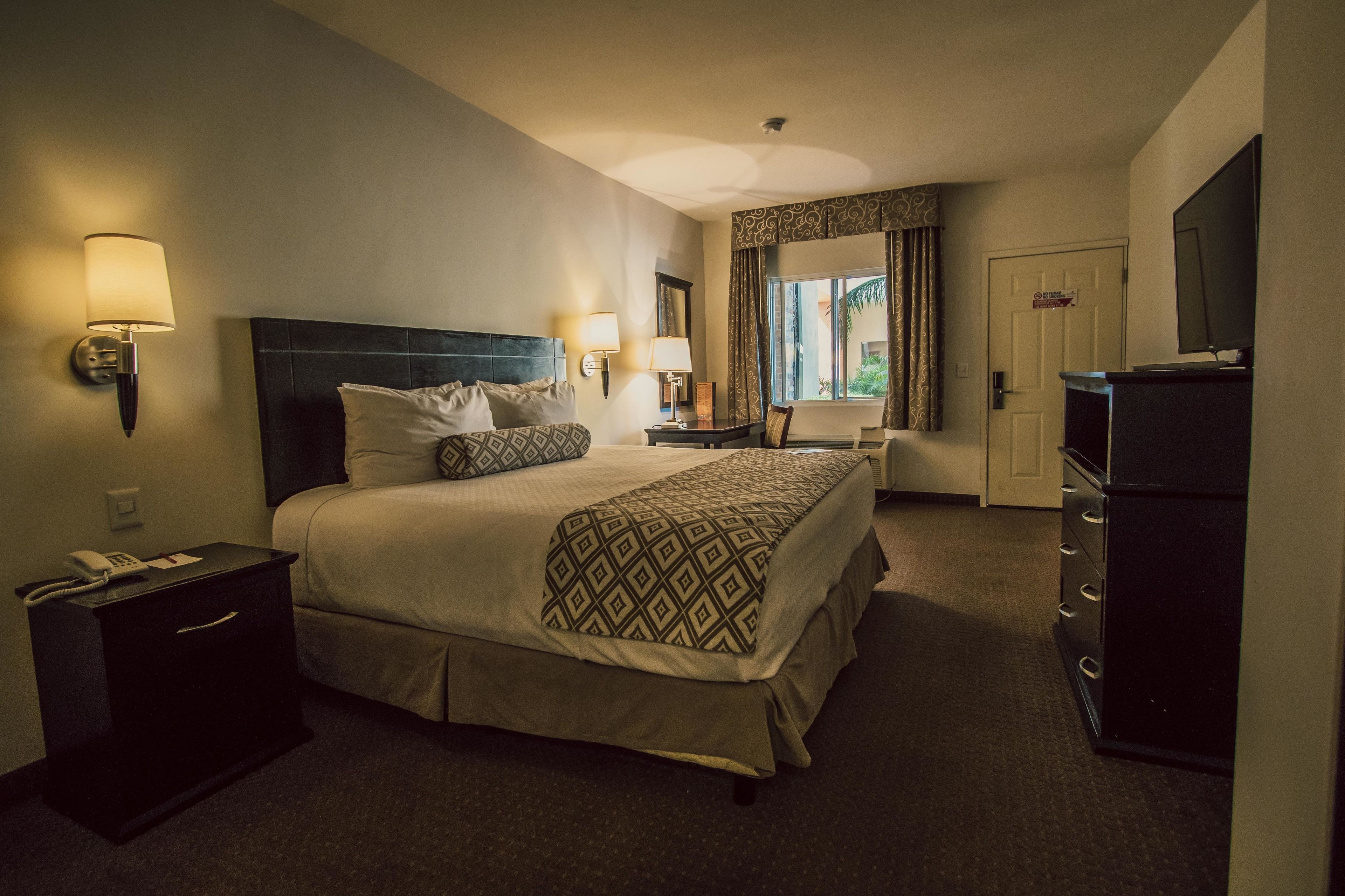 A hotel room with a large bed, bedside lamps, a desk, a dresser, and a TV.