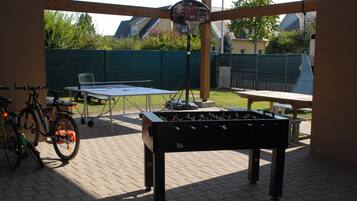 Un espacio recreativo al aire libre con una mesa de fútbol de mesa, una mesa de ping pong y una bicicleta.