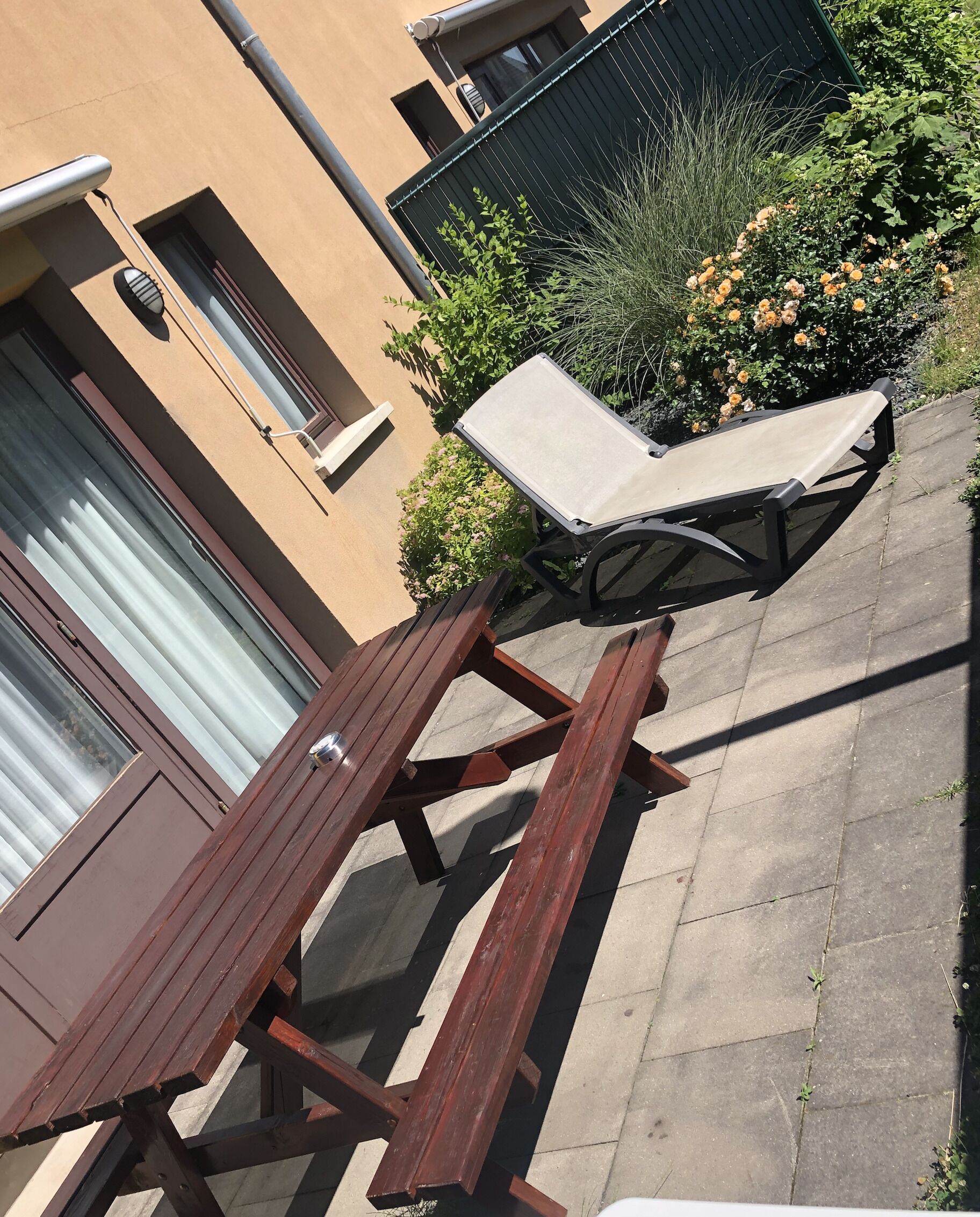 A wooden picnic table and a lounge chair in a courtyard with a building in the background.