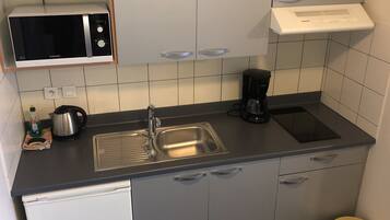 A compact kitchen with a microwave, coffee maker, and a small sink.