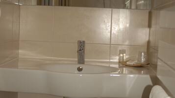 A bathroom with a large sink, a mirror, a shower, and a toilet.