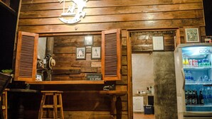 Angolo bar rustico con pareti in legno, cartello con l'orario di check-out e un frigorifero pieno di bevande.
