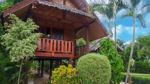Una casa in legno con un balcone, immersa nel verde e palme.