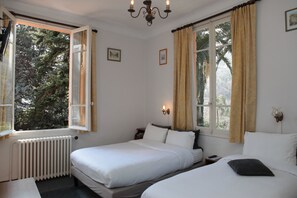 A bedroom with two beds, a radiator, and a window with curtains.