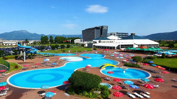 Un hotel con varias piscinas, tumbonas, sombrillas y montañas al fondo.