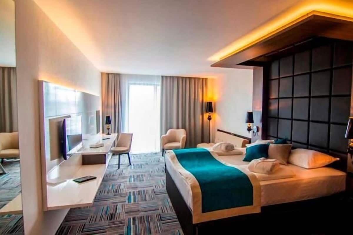 Ein Hotelzimmer mit Bett, Nachttischen, Schreibtisch, Stuhl und einem großen Fenster.