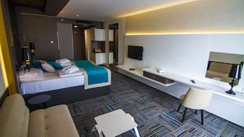 A modern hotel room with a bed, a sofa, a desk, and a TV.