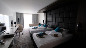 A hotel room with two beds, a desk, a chair, a TV, and a large window with curtains.