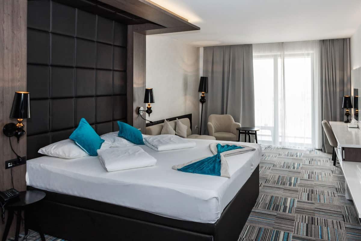 Ein Hotelzimmer mit einem großen Bett, zwei Nachttischen, einem Schreibtisch und einem Sessel.