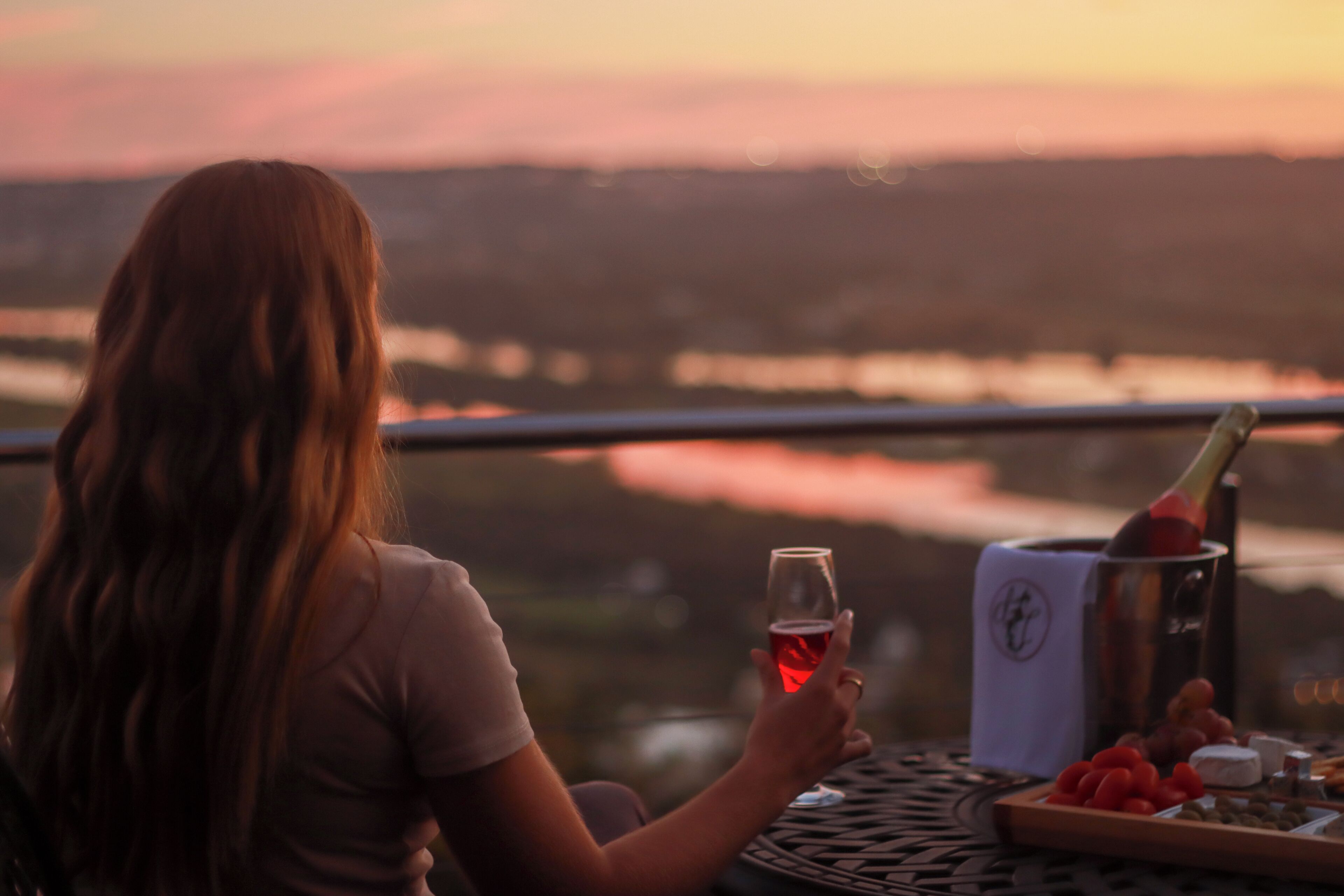 Una persona sentada a una mesa con una botella de champán, una copa de vino tinto y una bandeja de aperitivos.