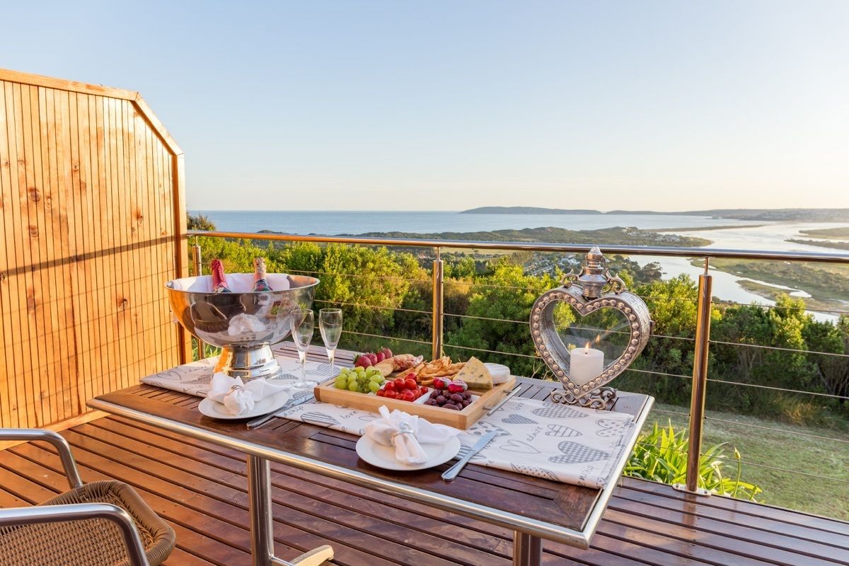 Una terraza de madera con una mesa dispuesta para una comida, con vistas a un paisaje que incluye un río y colinas.