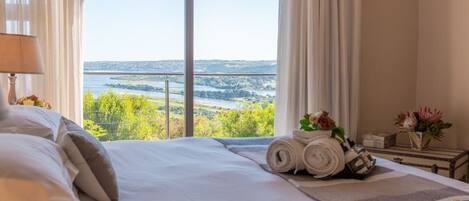 Habitación de hotel con una cama grande, vista a un cuerpo de agua y una ventana con cortinas.