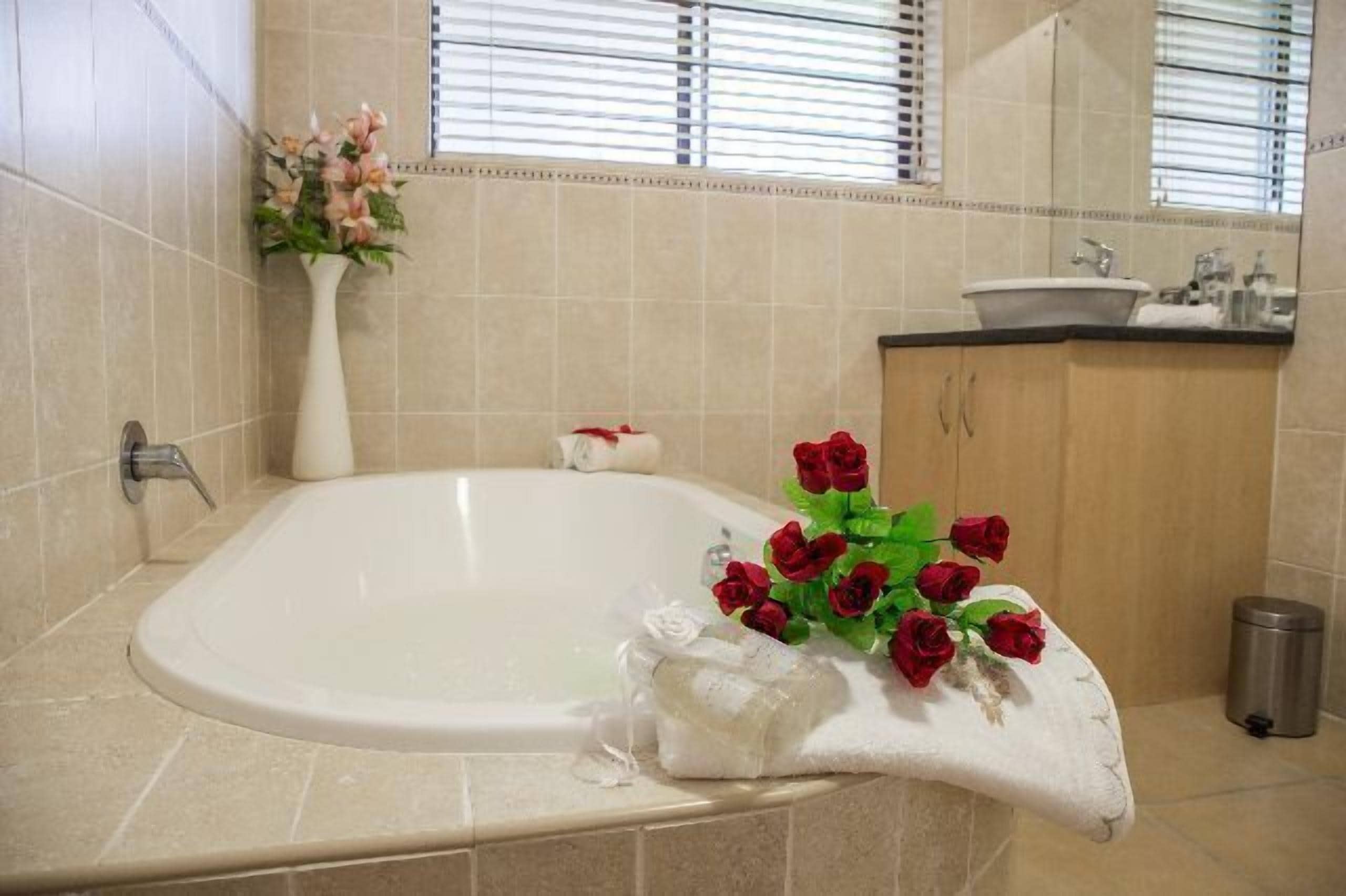 Un baño con una bañera, un lavamanos y un espejo. Hay un ramo de rosas rojas en el borde de la bañera.