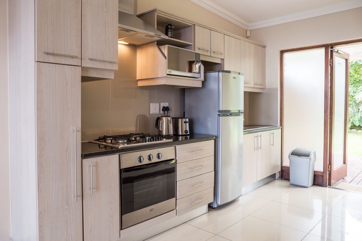 A modern kitchen with light wood cabinets, a stainless steel refrigerator, a gas stove, and a built-in oven.
