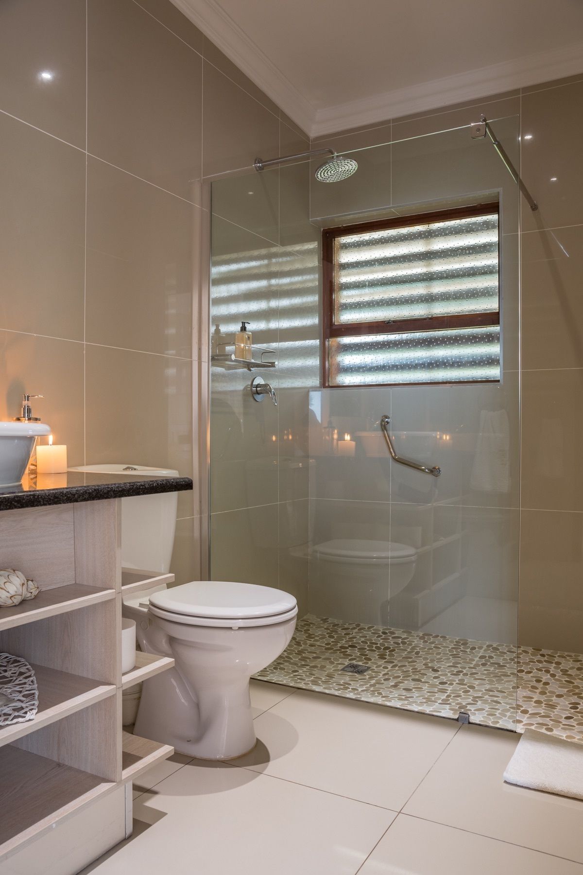 A modern bathroom with a glass-enclosed shower, a toilet, and a vanity with a sink and candle.