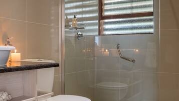Un baño moderno con cabina de ducha de vidrio, inodoro y tocador con lavamanos y vela.