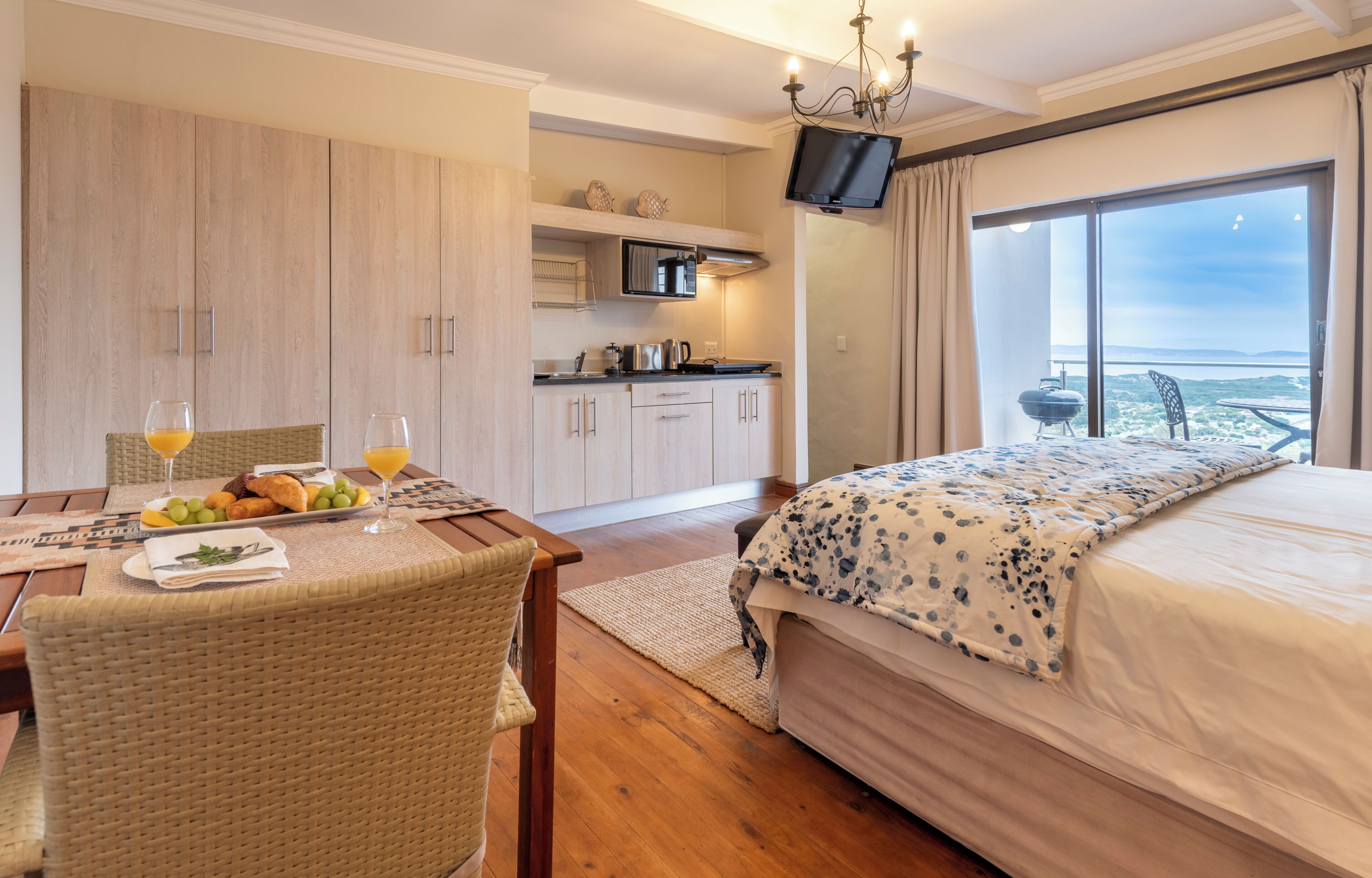 A hotel room with a bed, a dining table with breakfast, a kitchenette, and a TV.