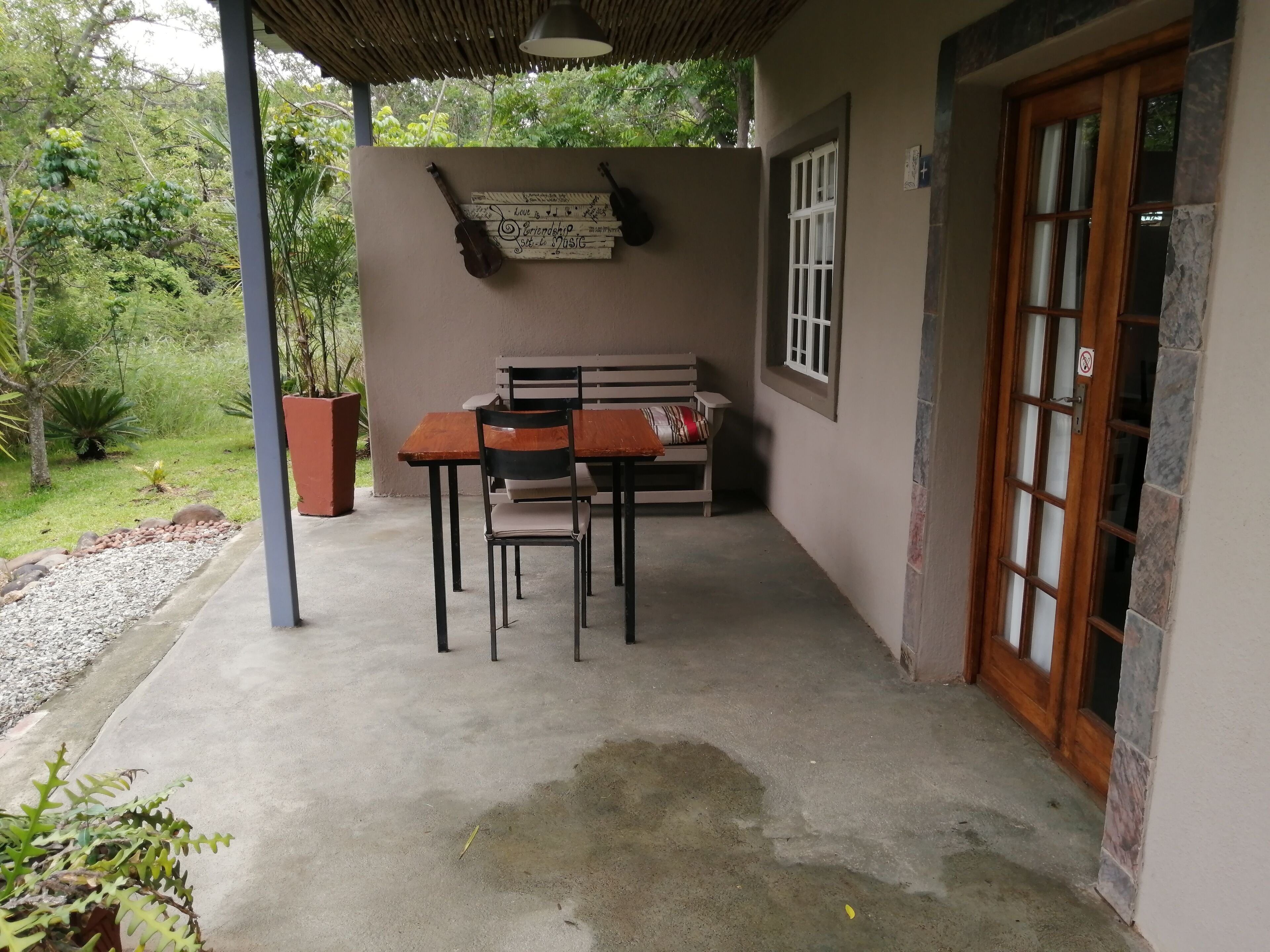 A covered outdoor seating area with a table and chairs, a bench, and a violin on the wall.