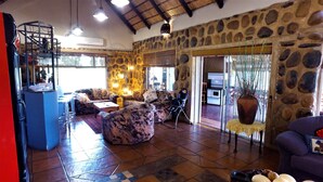 Zona d'estar àmplia amb una paret de pedra, un gran finestral i un conjunt de seients que inclou un sofà i cadires.