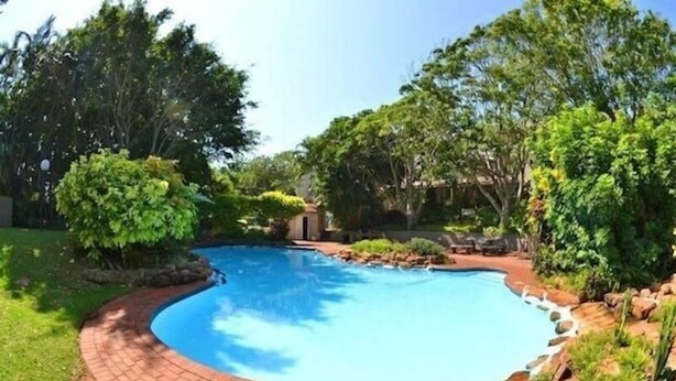 Piscina rodeada por um caminho de tijolos e vegetação exuberante.