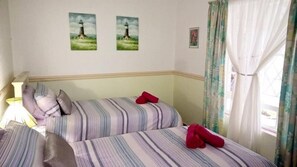 Une chambre avec deux lits, une literie à rayures, une lampe et deux tableaux représentant des phares accrochés au mur.