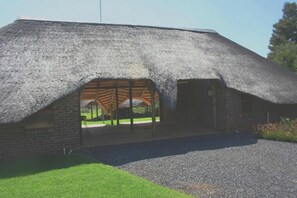 A thatched-roof building with a brick base, a covered outdoor area, and a gravel driveway.