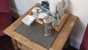 Et træbord med en bakke, der indeholder en kaffemaskine, kopper, en pakke lommevæv og en vævholder.