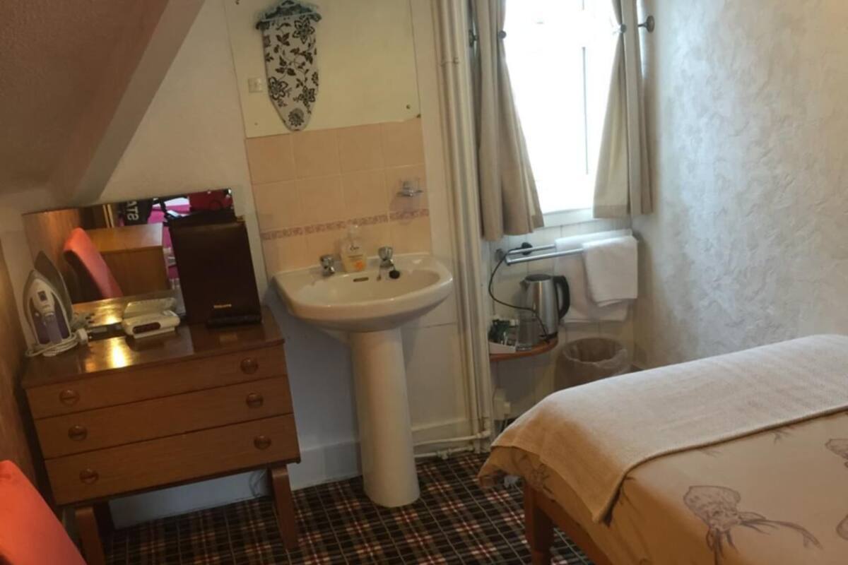 A hotel room with a bed, a desk, a chair, a sink, and a television.
