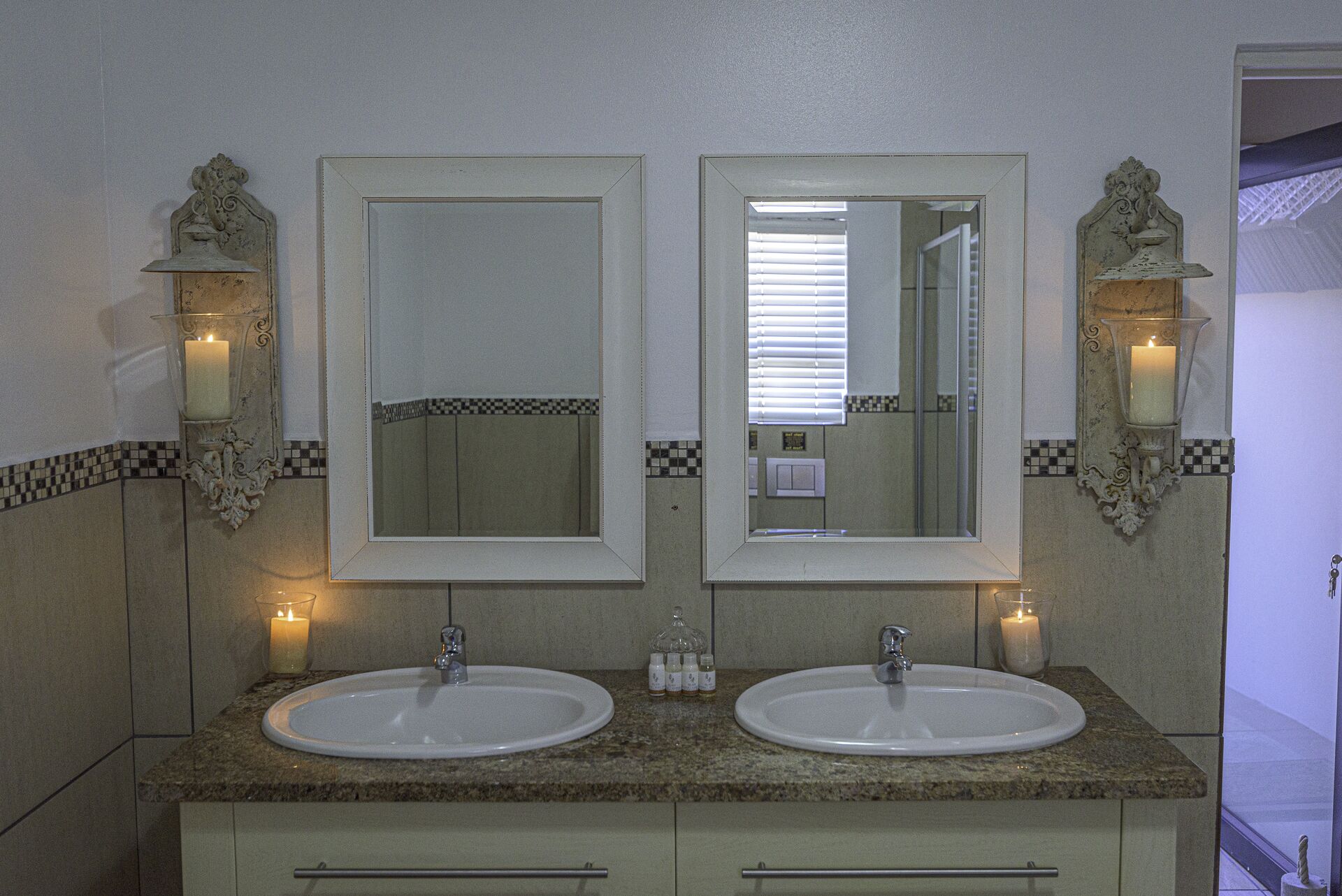 A bathroom with two sinks, two mirrors, and wall sconces with candles.