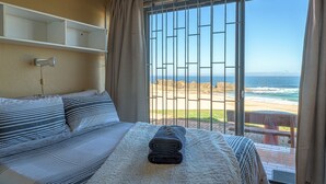 A hotel room with a bed, a view of the beach, and a window with metal bars. - Fynbos Golf & Country Estate (Eersterivierstrand)
