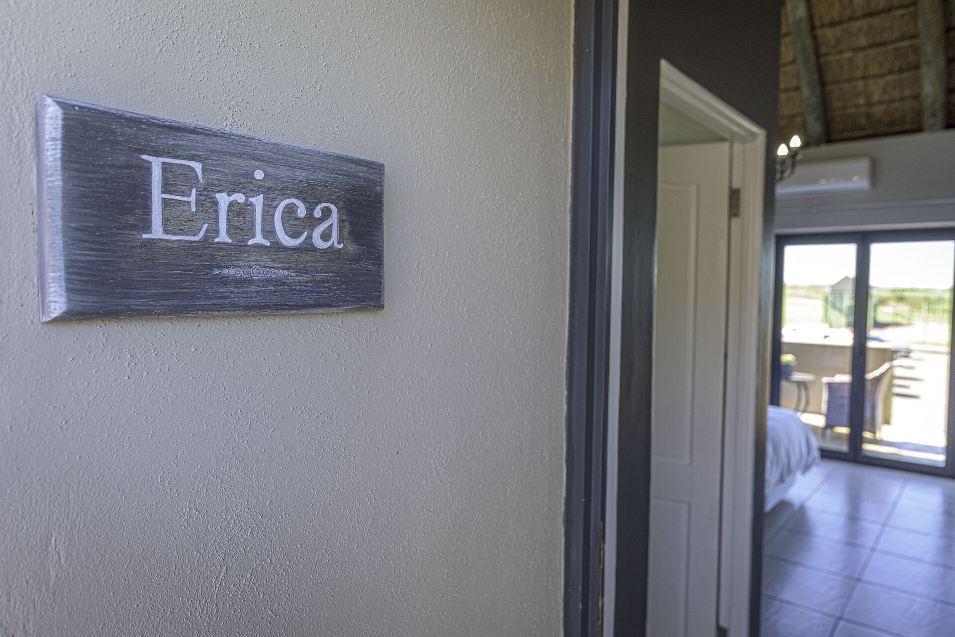 Un cartello con il nome 'Erica' su una parete strutturata, che indica l'ingresso in una stanza con vista su uno spazio esterno.