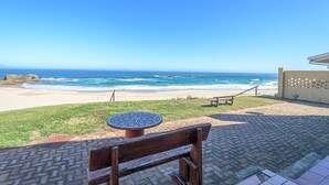 A beach view with a patio area featuring a wooden bench and a round table. - Fynbos Golf & Country Estate (Eersterivierstrand)