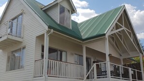 A two-story house with a green roof, a covered porch, and a staircase leading to the upper floor. - Knock Out View Clarens (Clarens)