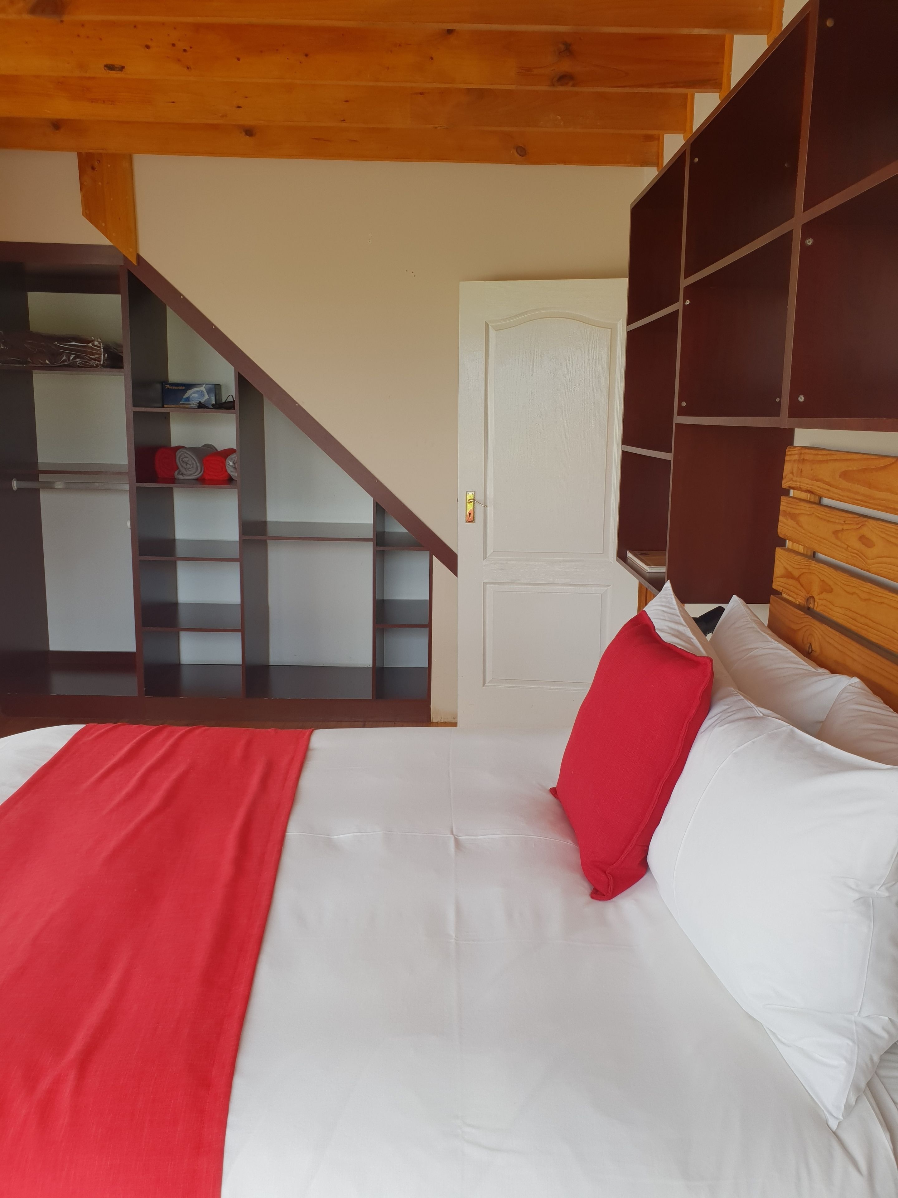 A bedroom with a bed, a wooden headboard, a red pillow, and a white bedspread.