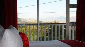 A bedroom with a bed, red and white pillows, and a balcony with a view of mountains. - Knock Out View Clarens (Clarens)