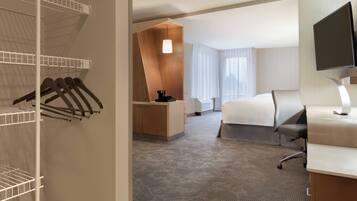 A hotel room with a bed, a desk, a TV, a bathroom, and a closet with hanging clothes.