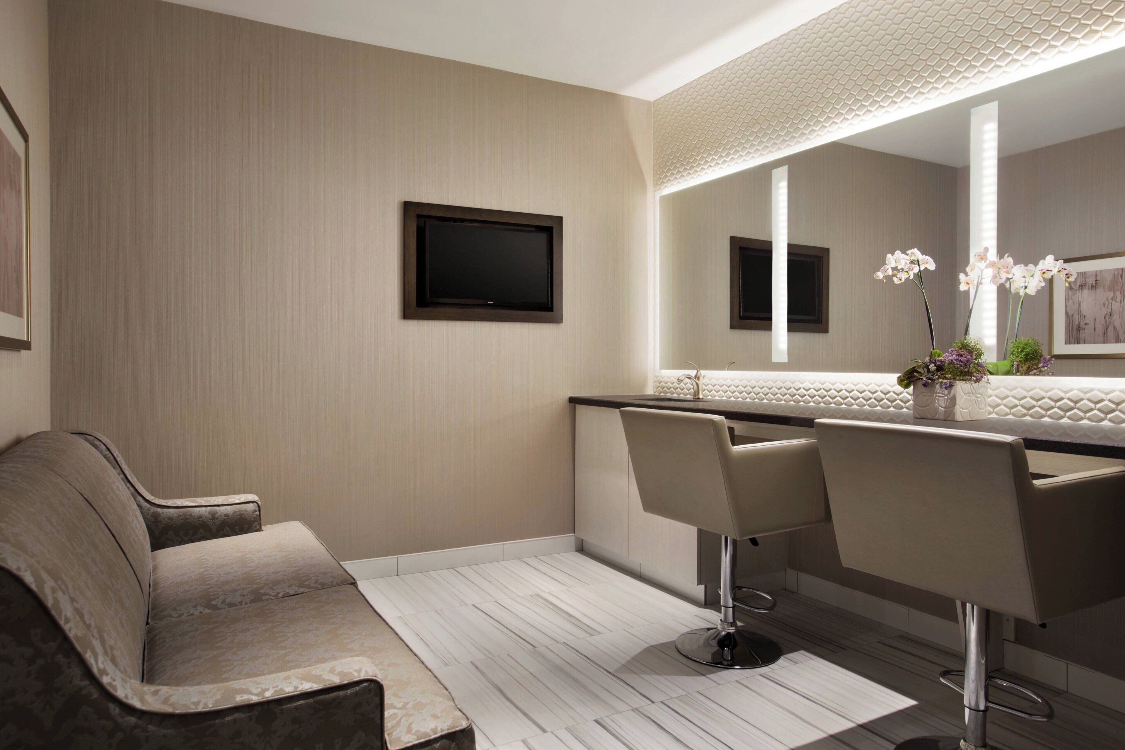 A modern bathroom with a large mirror, two bar stools, a sofa, and a flat-screen TV.