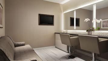 A modern bathroom with a large mirror, two bar stools, a sofa, and a flat-screen TV.