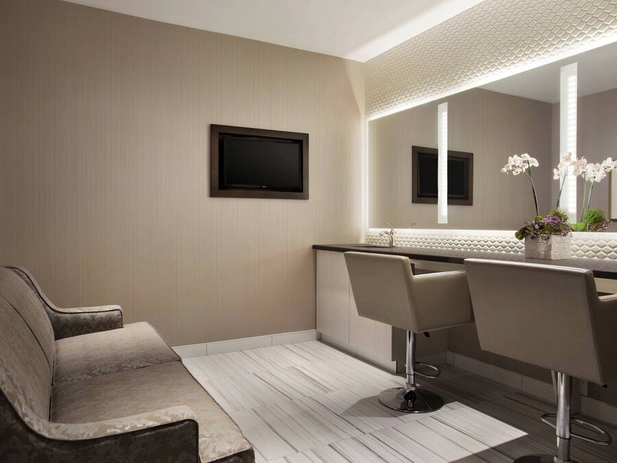 A modern bathroom with a large mirror, two bar stools, a sofa, and a flat-screen TV.