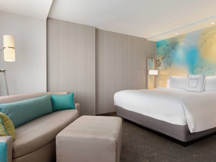 Quarto de hotel moderno com uma cama, um sofá, um abajur e uma parede texturizada.