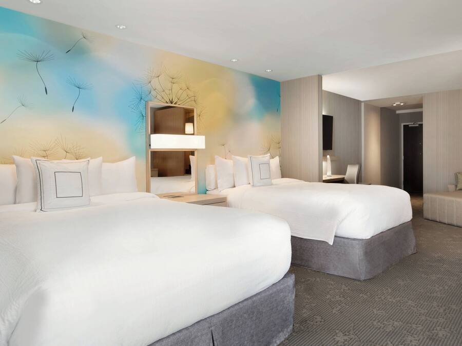 A modern hotel room with two large beds, a sitting area, and a large mirror.