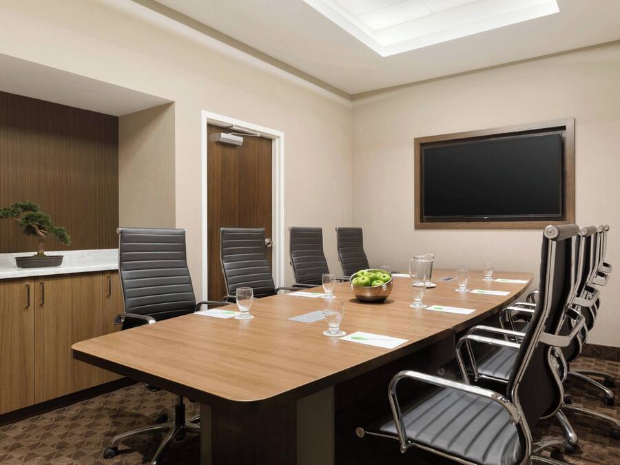 A conference room with a long table, black chairs, a potted plant, and a blackboard on the wall.