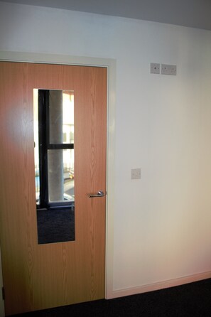 A room with a wooden door, a small window, and a white wall with two electrical outlets.