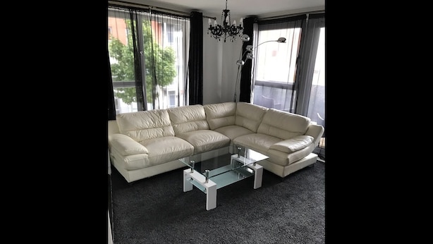 A modern living room with a L-shaped sectional sofa, a glass coffee table, and a chandelier.