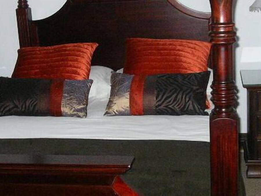 A four-poster bed with a dark wooden frame and a white bedspread. There are two nightstands with lamps on either side of the bed.