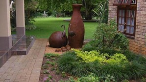 Un jardin agrémenté d’un grand vase et d’une sculpture, un bâtiment en briques doté d’une fenêtre, et un chemin pavé.