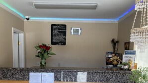 A reception desk with a digital clock, a sign with check-in times, and a flower vase. - Budget Motel (Mountain View)